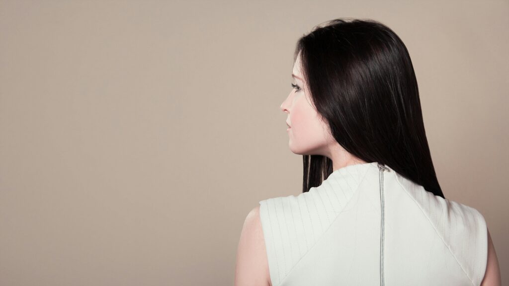 Profile view of a brunette woman in white attire indoors on a neutral background.